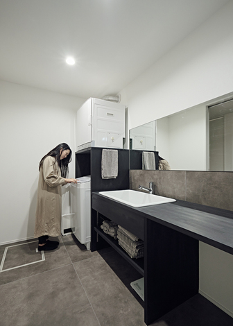 洗濯機の収納と一体化した造作の洗面スペース。黒で着色した木製で、壁にはフロア用のタイルを貼ってある。化粧台は２人並んで使える広さにし、椅子を置いてスキンケアやメイクがゆっくりできるようになっている