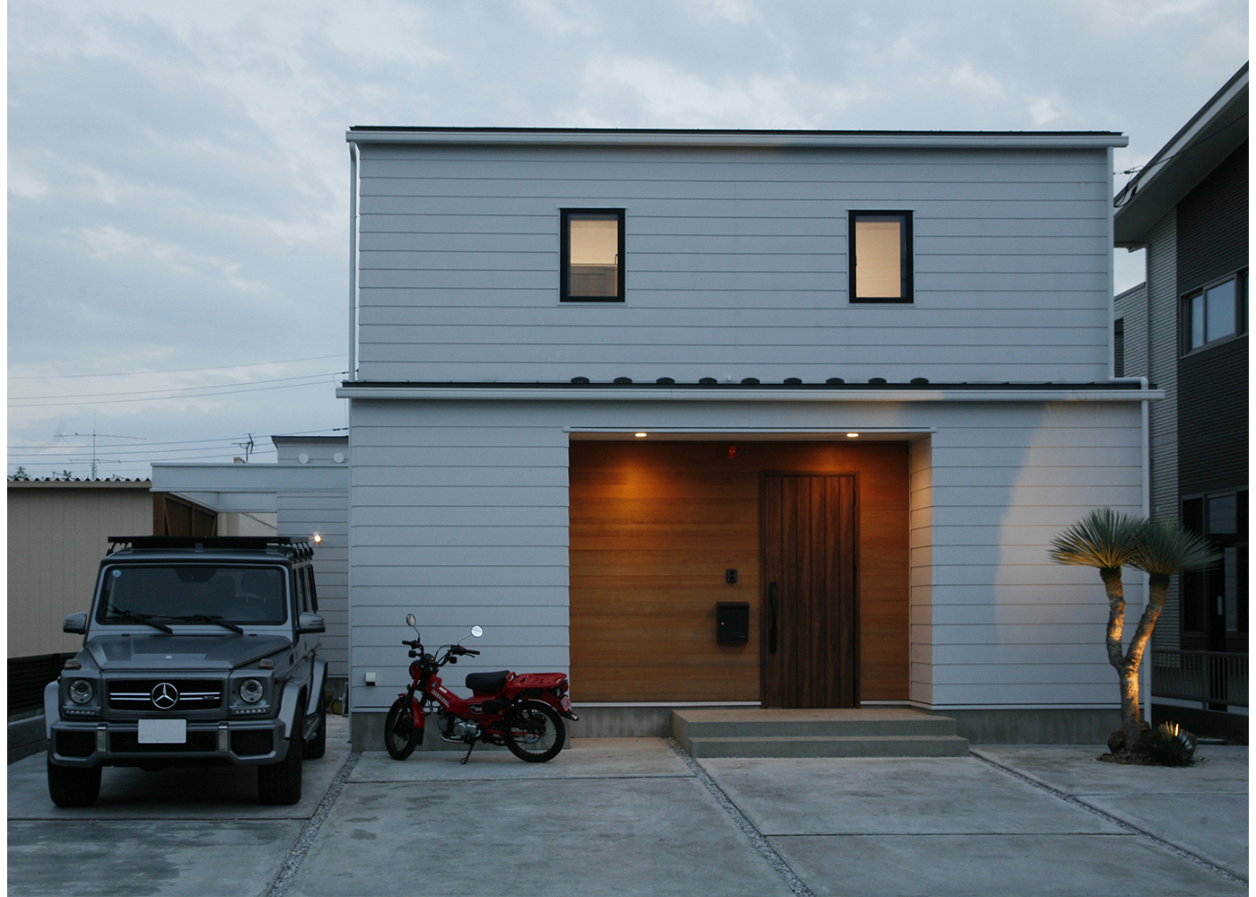 タツホーム・竜建｜シンプルでモダンな外観の住宅。木製ドアとコンクリートの組み合わせが洗練された印象を与え、落ち着いた雰囲気を演出している。