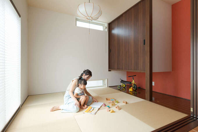 リビングとフラットにつながる和室。西面からの視線を避けるため、上下2か所に横長の窓を設けた。吊り押入で空間がより広く感じられる。弁柄色のクロスと和の照明は奥さまのこだわり。引き戸で仕切ることもできるので、ゲストの寝室としても使える