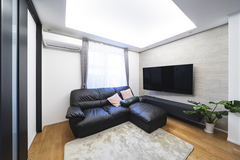 ブラックのソファが置かれたモダンなリビング。壁には大型のテレビが設置され、観葉植物がアクセントを添える。リラックスできるシンプルな空間設計。