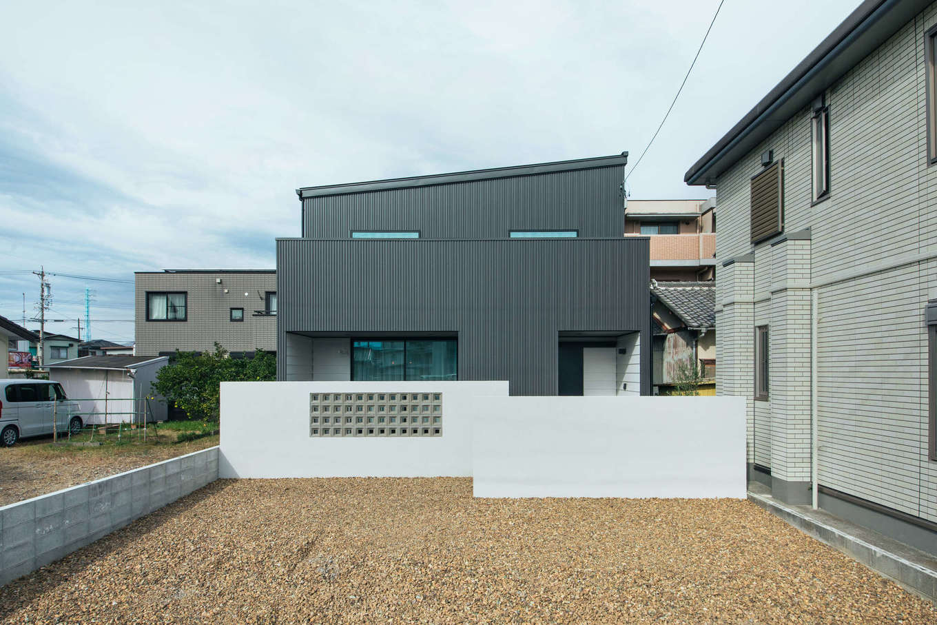 DAITOKU（大得工務店）【デザイン住宅、子育て、間取り】シンプルモダンなデザインが特徴の外観。人通りが多いため、ブロックウォールで緩やかに目隠しを施した。塀の内側のエントランスはタイルデッキの広い庭になっている