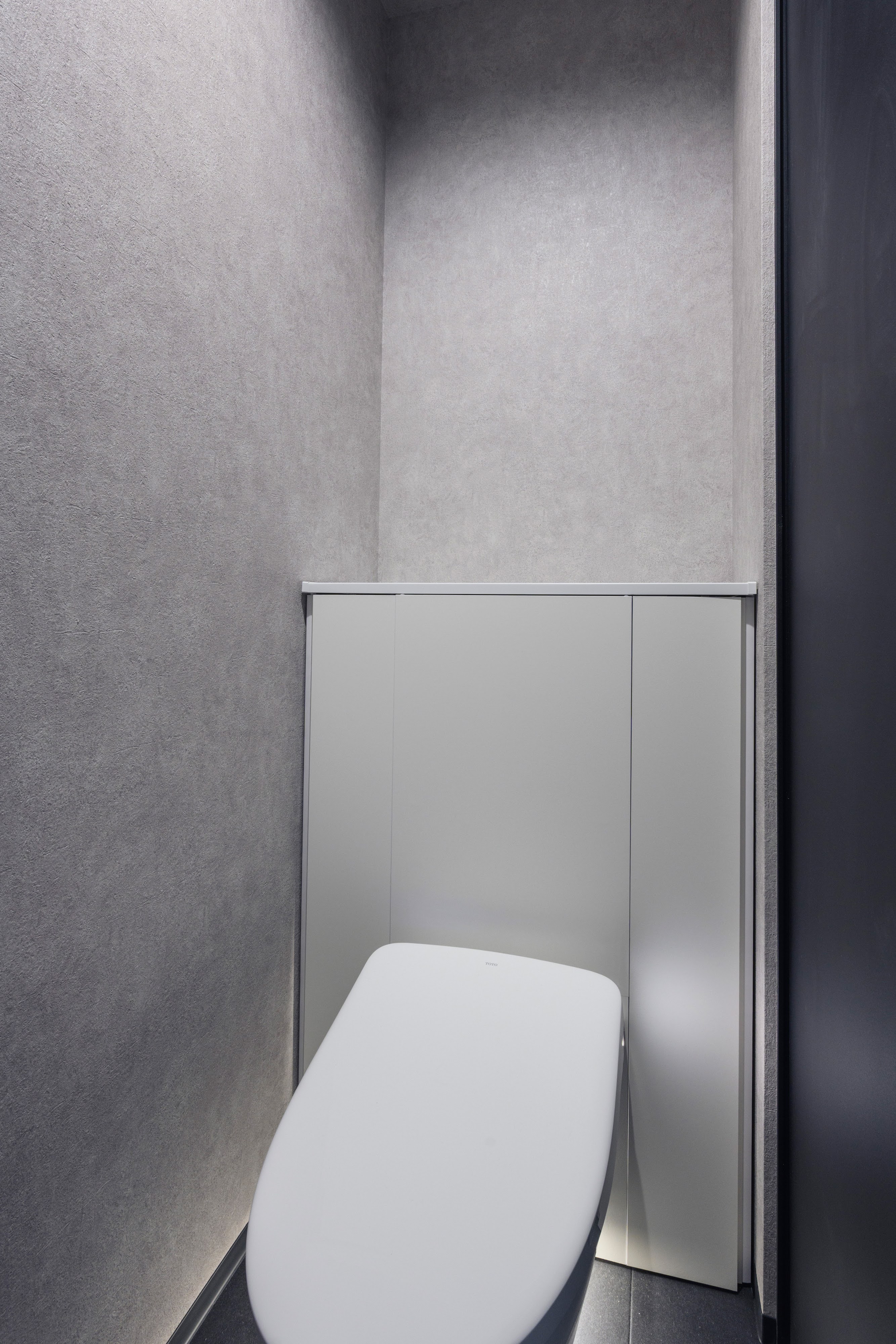 K-rise｜ミニマルなデザインのトイレ空間。シンプルな白とグレーの色調がモダンな印象を与え、清潔感を感じさせる。この狭さでのデザイン性が非常に秀逸である。