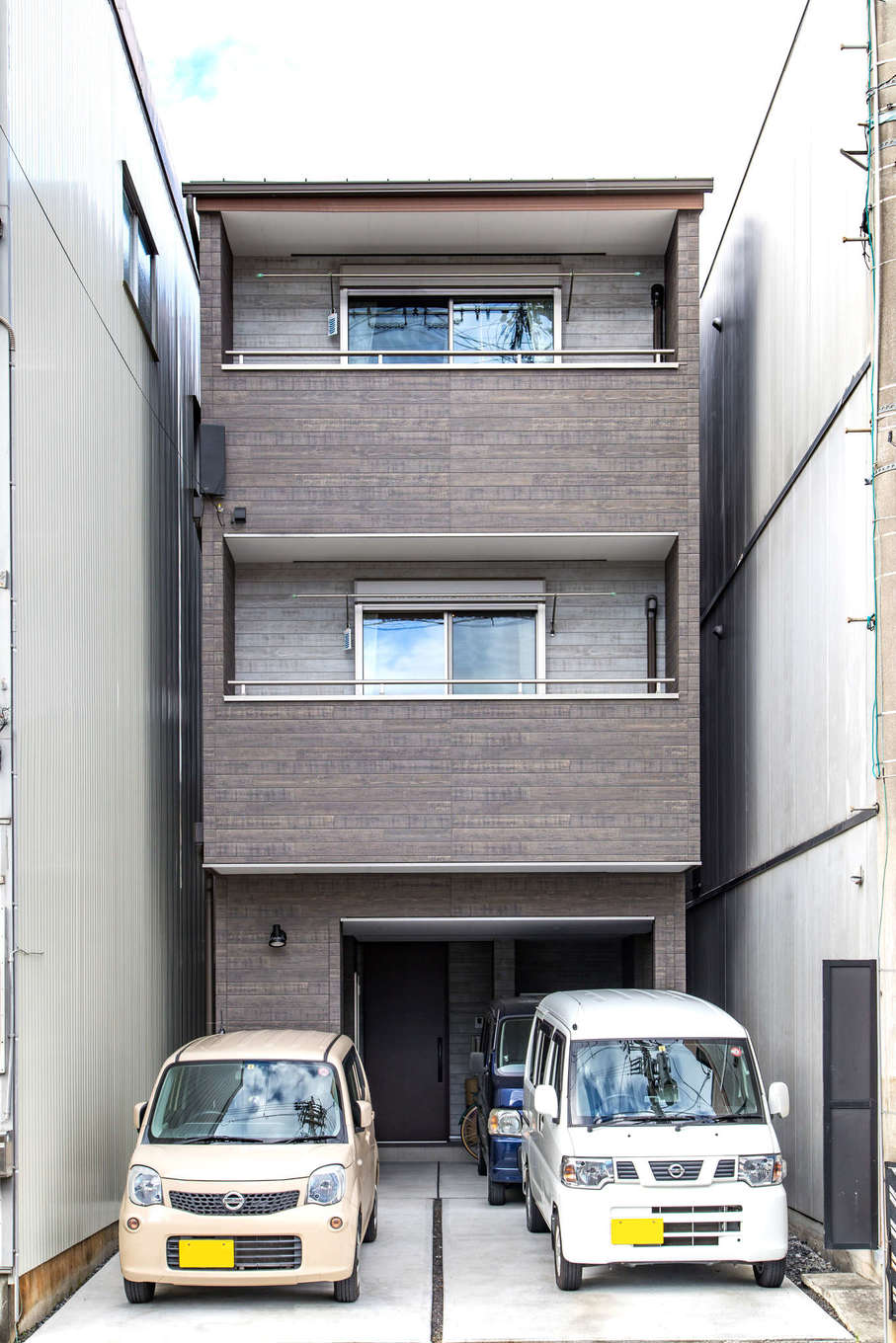 建築システム（狭小住宅専門店）【収納力、狭小住宅、ガレージ】隣り合う家との隙間はわずか。この敷地に3台駐車可能な3階建てを実現。外観はシックで落ち着いた木目調のサイディングでまとめた
