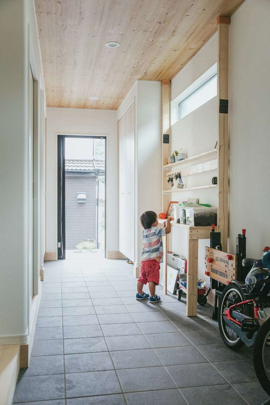 子育て安心住宅 Design Craft Office【デザイン住宅、子育て、平屋】“ファミクロ”＆ランドリーと、キッチン、リビングのそれぞれに直結する玄関土間。壁面のラックは奥さまがDIYで取り付けたもの。子どもが土間で三輪車遊びをすることもあるそう