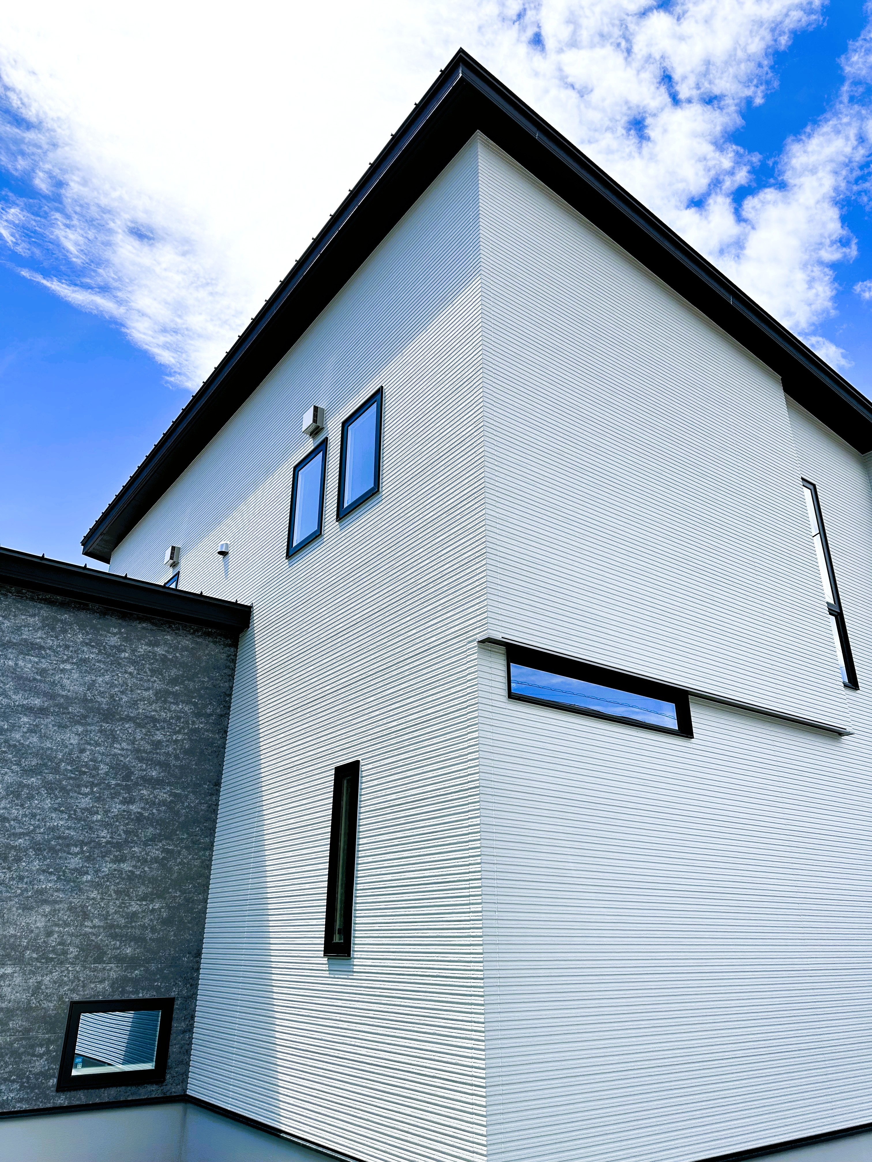 イシカワ 岐阜支店｜モダンでシャープなラインの外観が特徴的な住宅。シンプルな色調でまとめられており、垂直線が建物を引き立てるクールなデザイン。青空を背景に、美しいシルエットが際立つ。