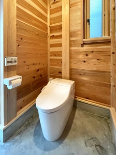 ウッド素材で温かみのあるトイレ空間。自然光が差し込む窓があり、心地よい雰囲気が漂う。外からのトイレなので土間使用。