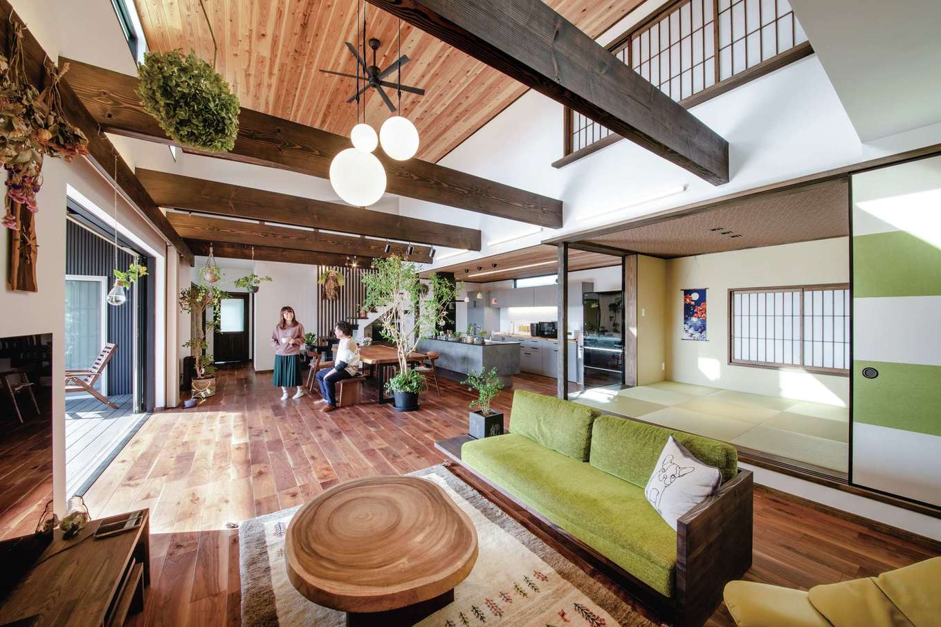 丸洋建設 ハウスオブハウス【デザイン住宅、自然素材、平屋】30畳を超えるダイナミックな吹抜けのLDK。和モダンな雰囲気にするため、梁や建具を黒く塗装し、壁は漆喰を使用した。小上がりの和室は間仕切りも可能で、ゲストの寝室としても使える。グリーンが差し色に
