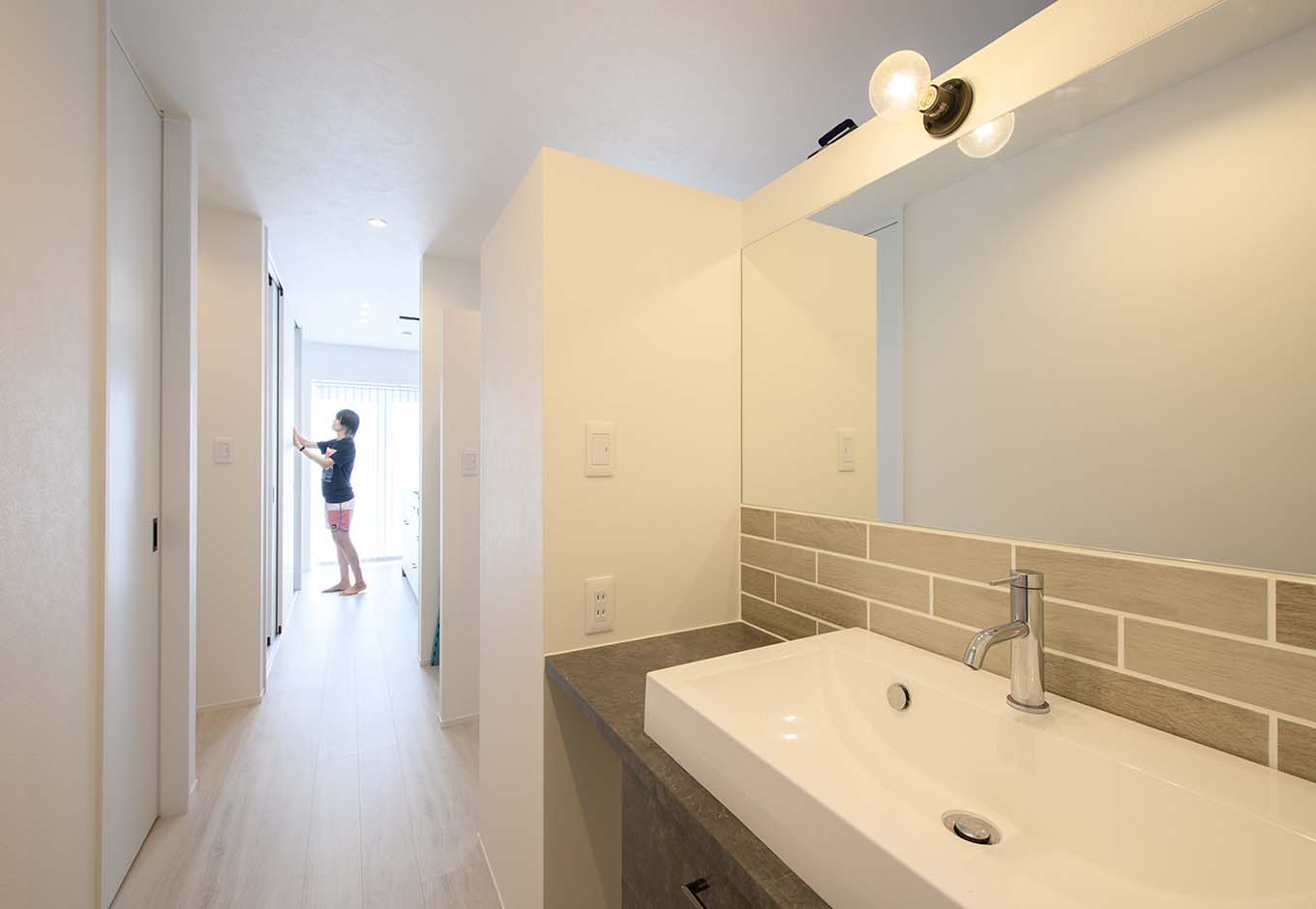 平屋建築ブルーハウス【デザイン住宅、間取り、建築家】脱衣室の外にある独立型の洗面。誰かがお風呂に入っていても、気兼ねなく洗面を使うことができる。また、玄関やトイレの近くに配置することで、使い勝手もより高まった