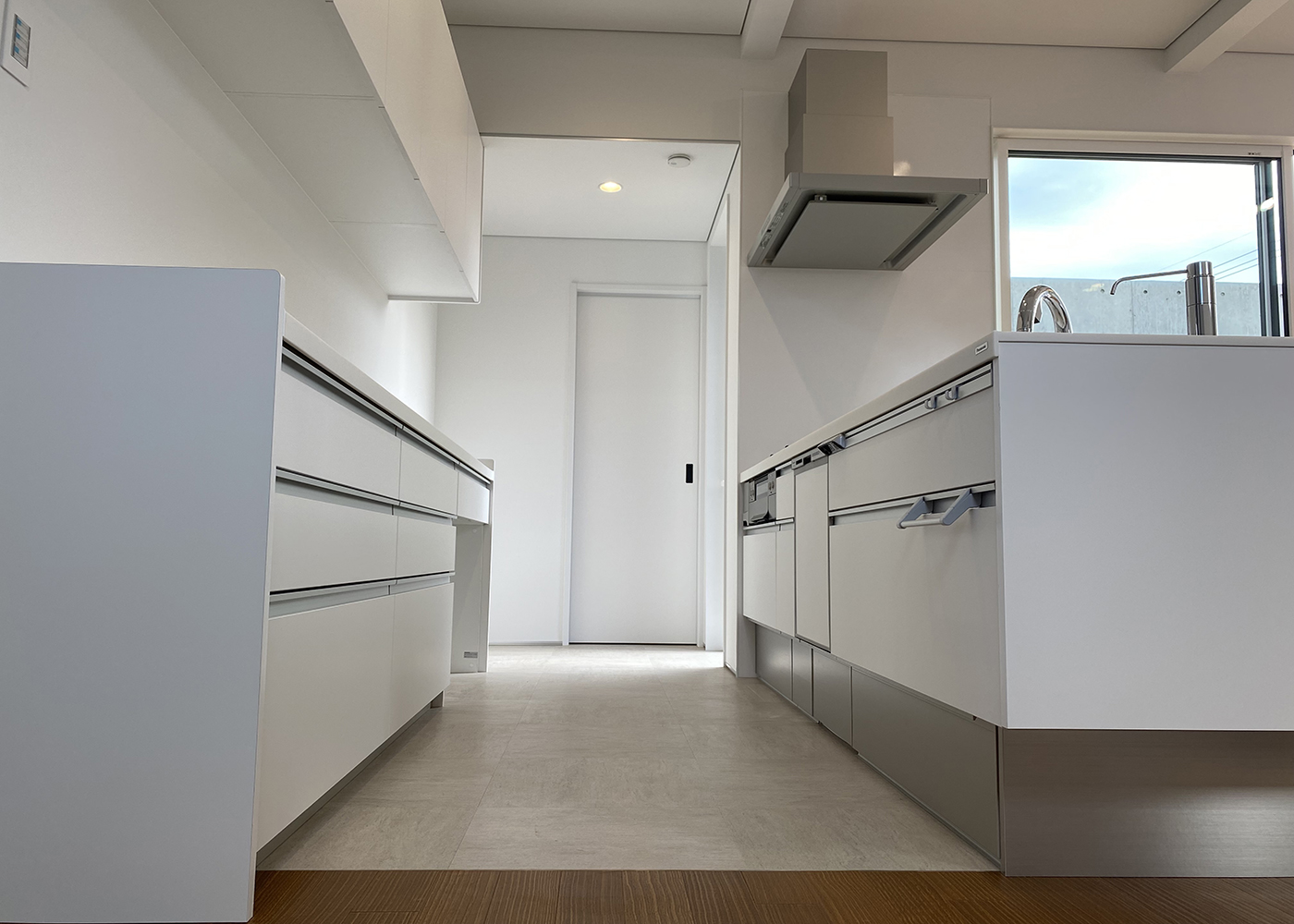 ぽっくハウス豊橋店（東海ハウス豊橋）【デザイン住宅、趣味、スキップフロア】キッチンとカップボードは白一色で統一。まっすぐ進むとタイルデッキへ出る扉があり、奥の白い引き戸は脱衣室につながっている