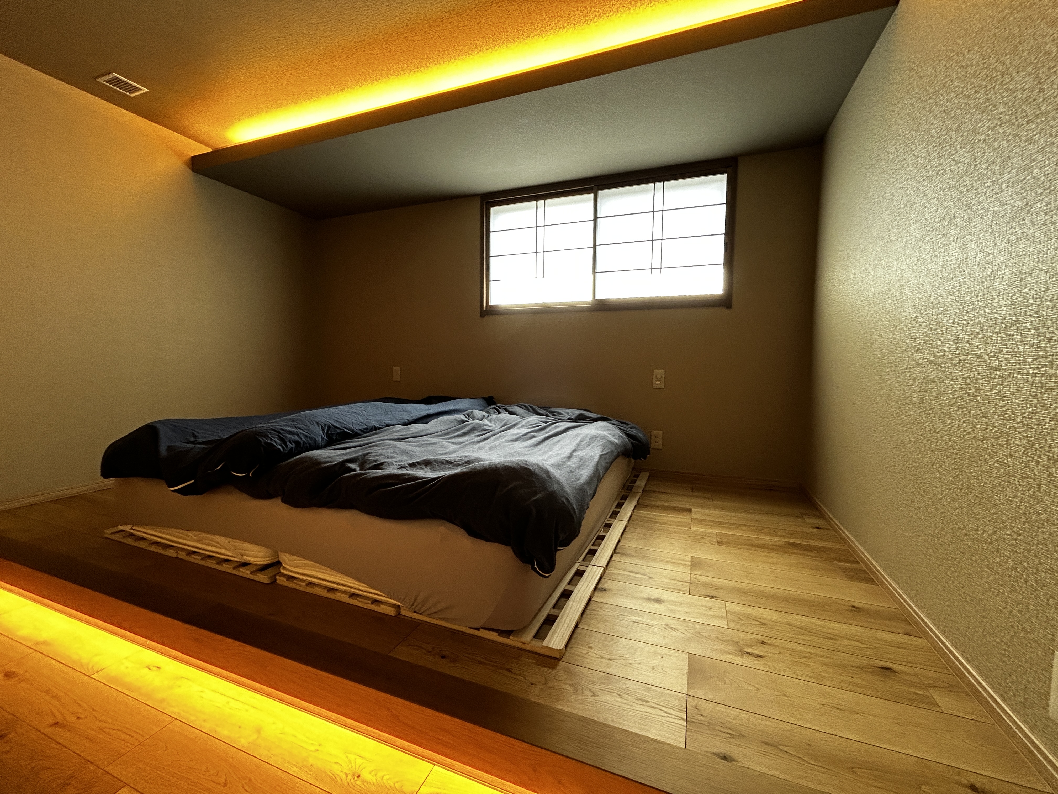 パナソニックホームズ中部第一支社 愛知第一支店・愛知第二支店｜温かみのあるライトで照らされた小上がりのスペース。心地よい床材と落ち着いた壁の色合いが、リラックスできる空間を演出している。