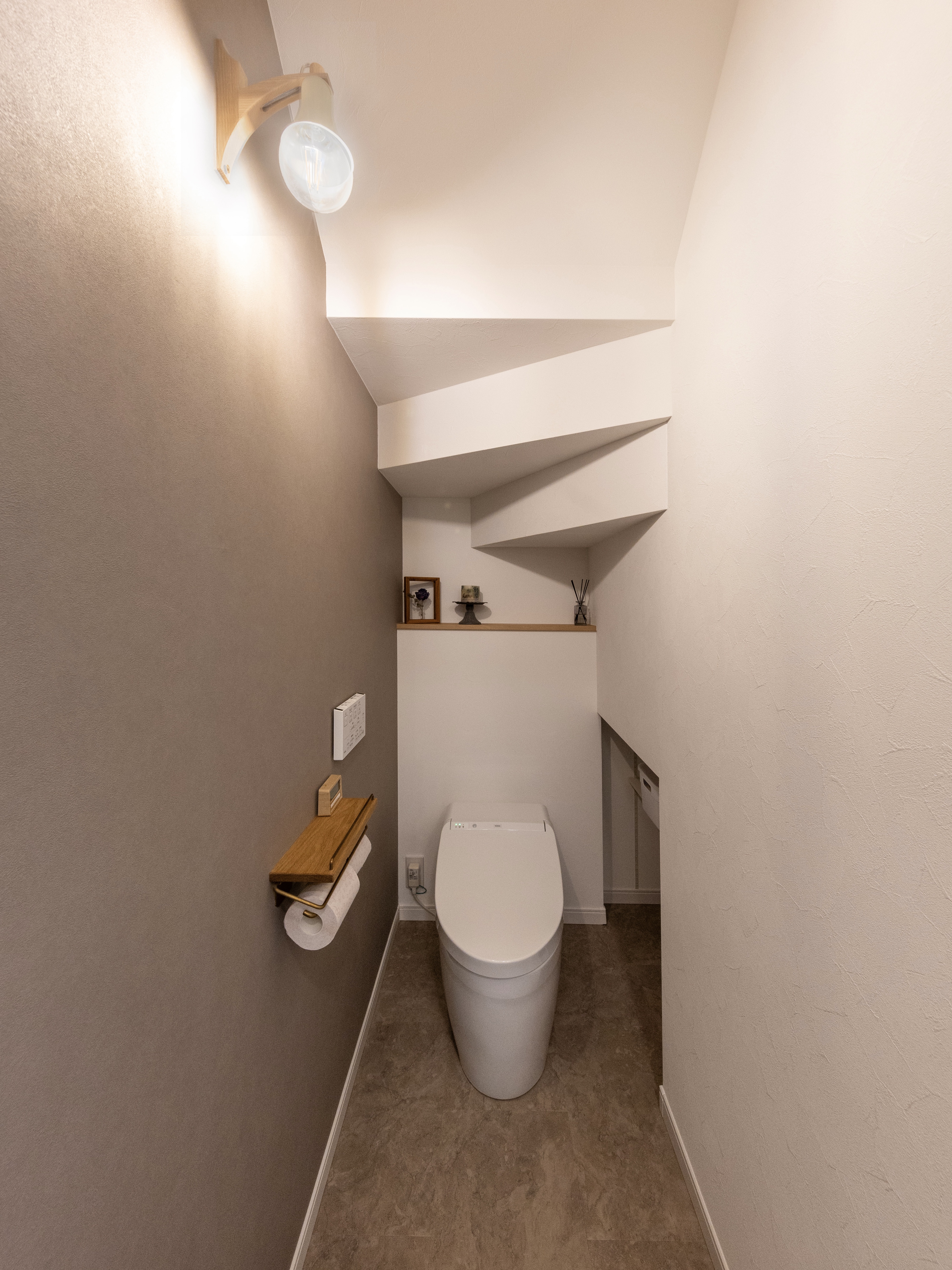 エスホーム｜階段下を利用した一階トイレ。コンパクトながらも機能的な設計で、落ち着いた照明がリラックスできる雰囲気を演出。