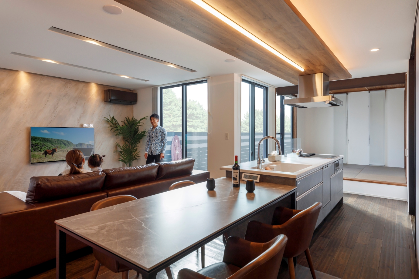 nattoku住宅【デザイン住宅、子育て、間取り】L字型のL D Kに接するように庭を設け、人目を気にすることなく開放感と明るさを室内に招きつつ、奥さまが希望した「どこにいても家族を感じるLDK」を実現。吟味した照明計画により提供される優しい光が、ほっとする落ち着きを添えている。キッチン収納は半透明の扉で家電や食器を隠すことにより、スッキリをキープ。右手手前の宿題用カウンターの壁は、全面をマグネットボードに