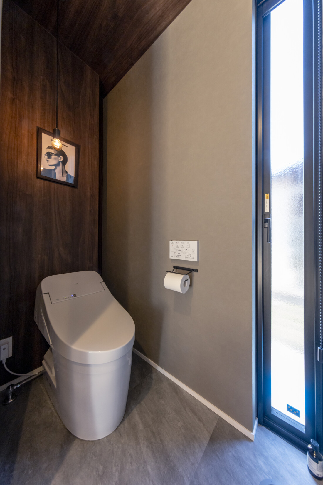 チェックハウス｜落ち着いた照明のトイレ空間。スタイリッシュなタンクレストイレが設置され、壁のアートがアクセントに