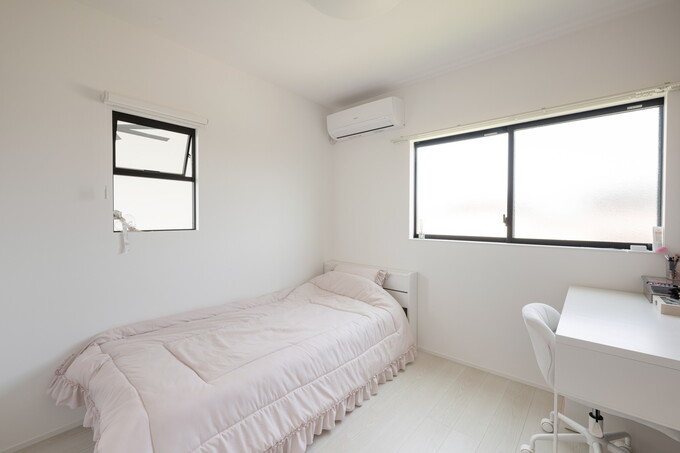 明るくシンプルな内装の子供部屋。自然光が差し込み、落ち着いたベッドとワークスペースが配置され、快適な時間を過ごせる空間である。