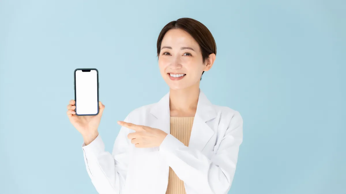 白衣を着た女性がスマホを持っている