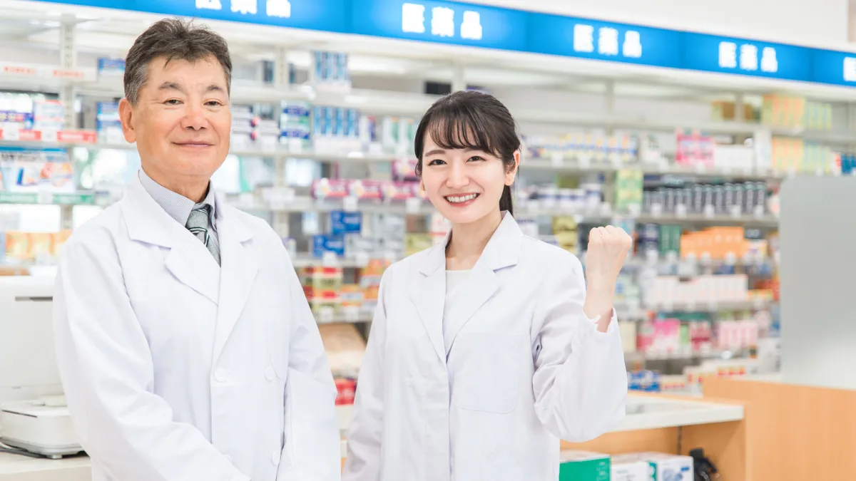 白衣を着た女性と男性
女性は笑顔でガッツポーズをしている。背景には医薬品の文字