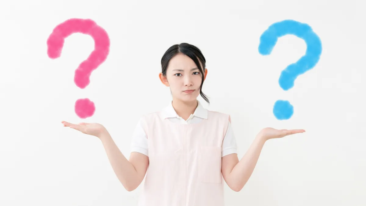 白衣を着た女性が青と赤のはてなをもっている