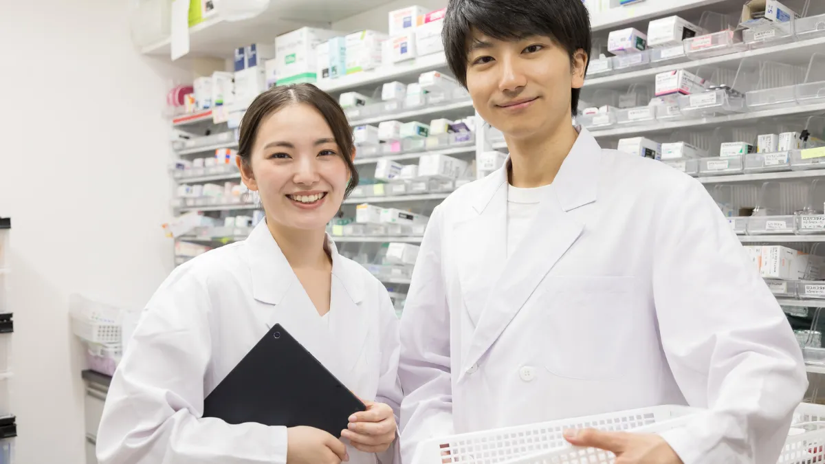 笑顔の白衣を着た女性と男性、背景は薬がたくさんある
