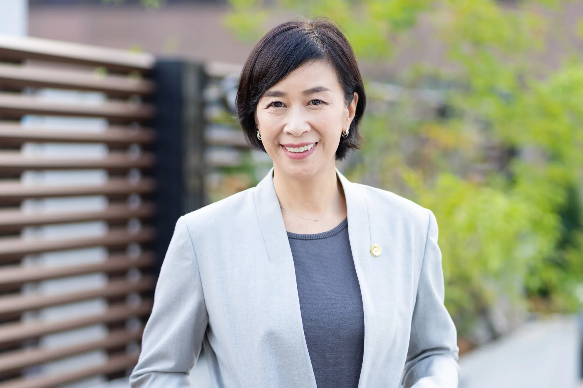 スーツを着た中年の女性が笑顔で立っている