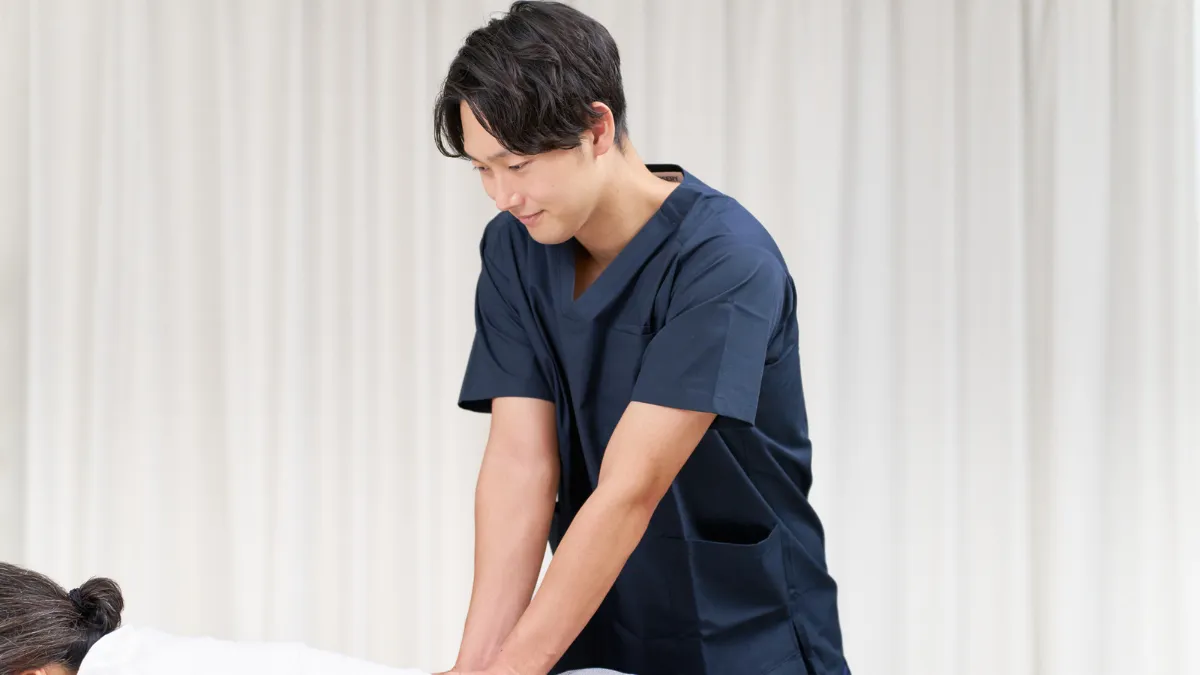 白衣を着た男性が寝ている人の背中をマッサージしている