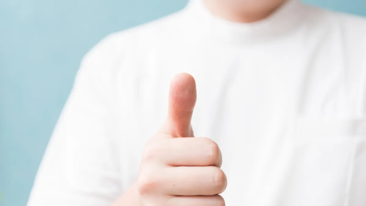 白衣を着た人が親指をたててグーサインをしている