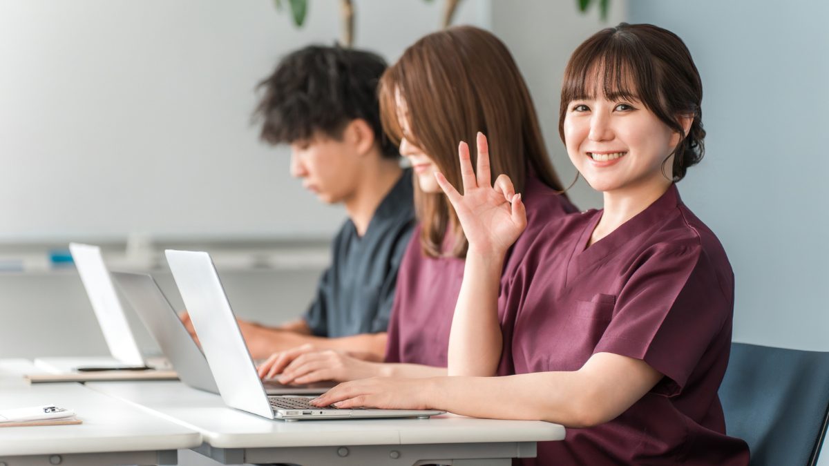 白衣を着た女性と男性が並んで座っていてそのうちの1人が指でグッドマークを作っている