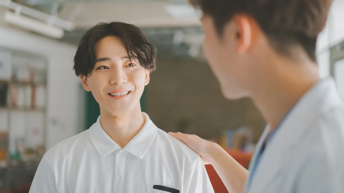 白衣を着た男性が若手と思われる男性の肩に手を置いている