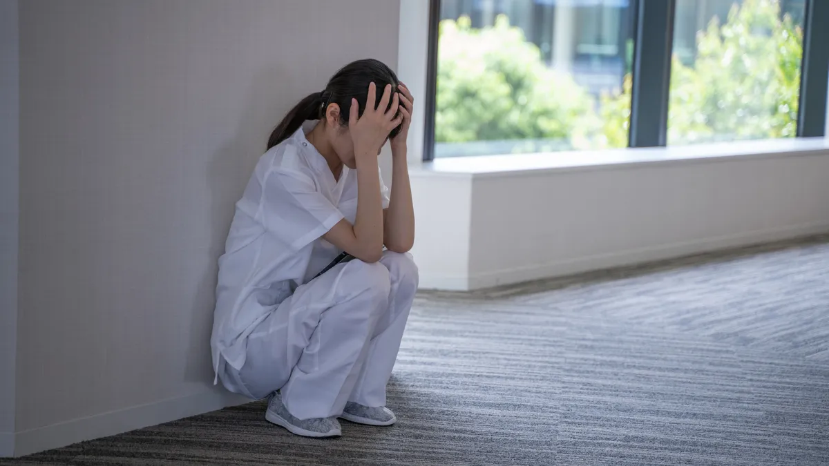 白衣をきた女性が廊下で頭を抱えてしゃがんでいる