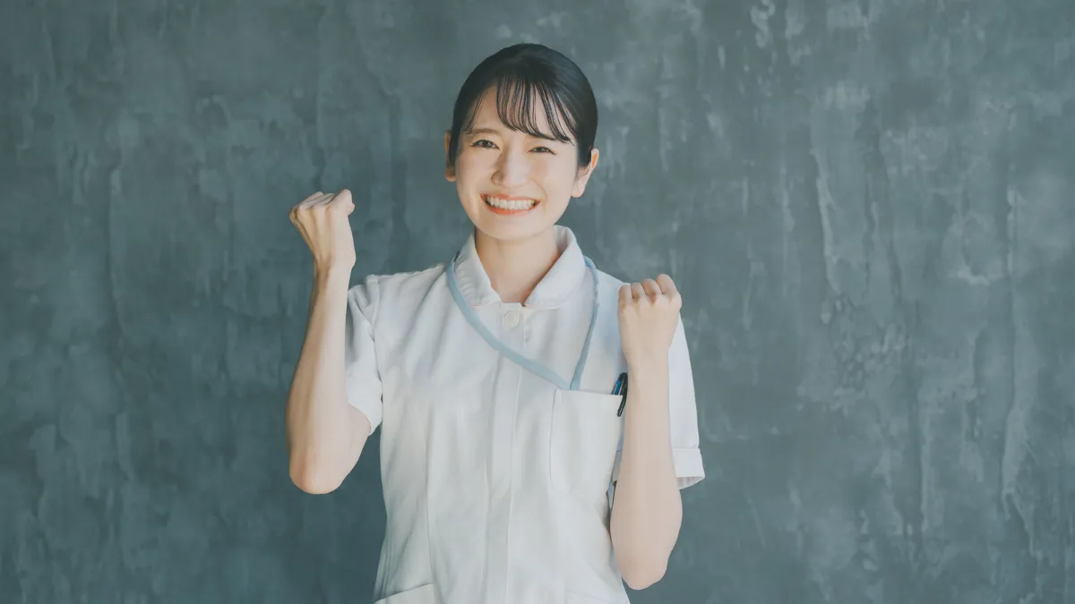 白衣を着た女性が笑顔でガッツポーズをしている