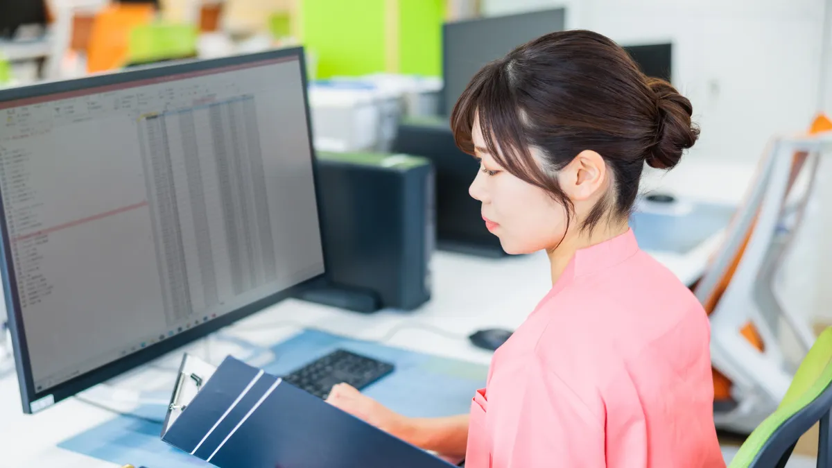 スクラブを着た女性がパソコンの前でタブレットを眺めてる