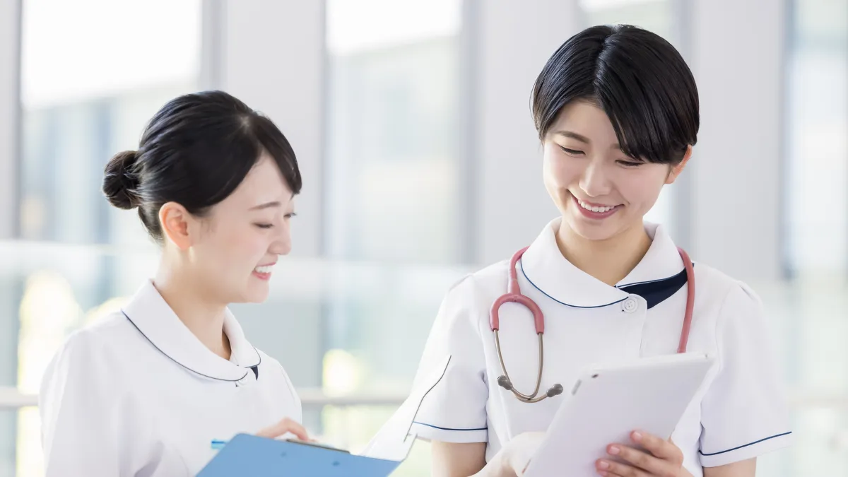 白衣を着た若い女性と中堅くらいの女性がバンを見ながら会話している