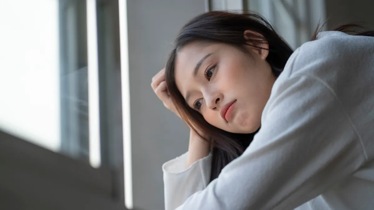 暗い顔をした女性が窓際で頭を抱えている