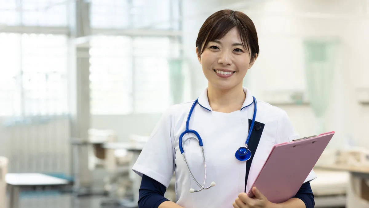 白衣を着た女性が聴診器を首にかけて笑顔でこちらを向いている