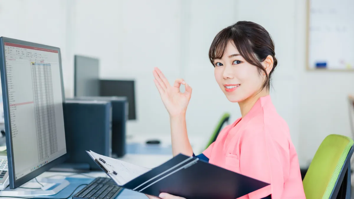 スクラブを着た女性がパソコンの前で〇を作ってる