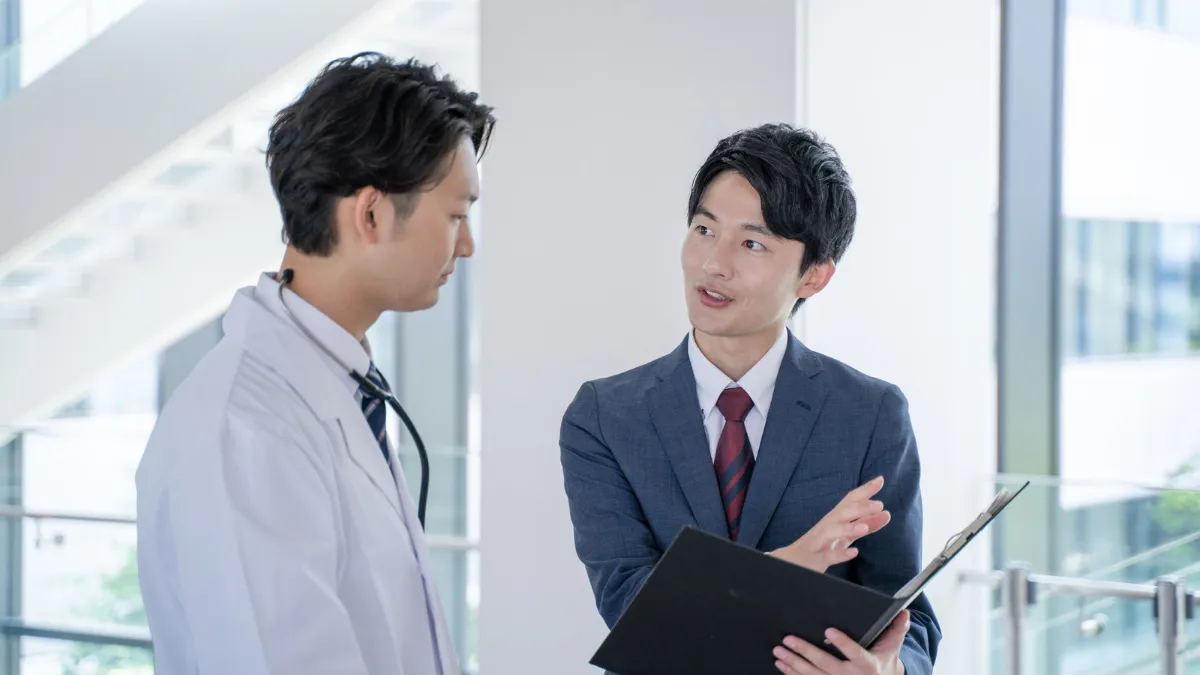 スーツの男性が白衣を着た男性に説明してる