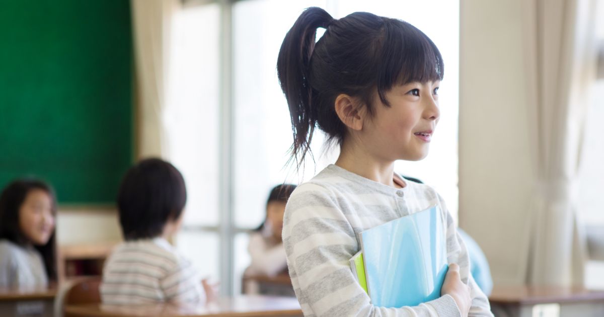 教室で教科書を胸に抱えている10歳女子
