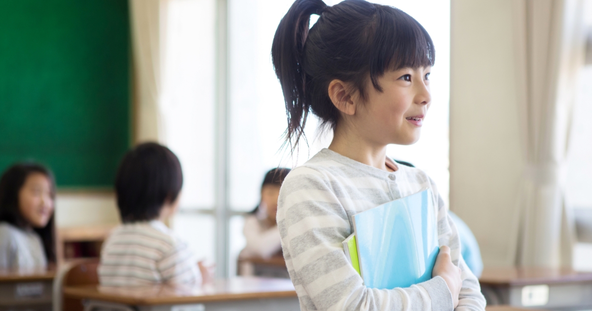 教室でファイルを抱えて微笑むポニーテールの女の子