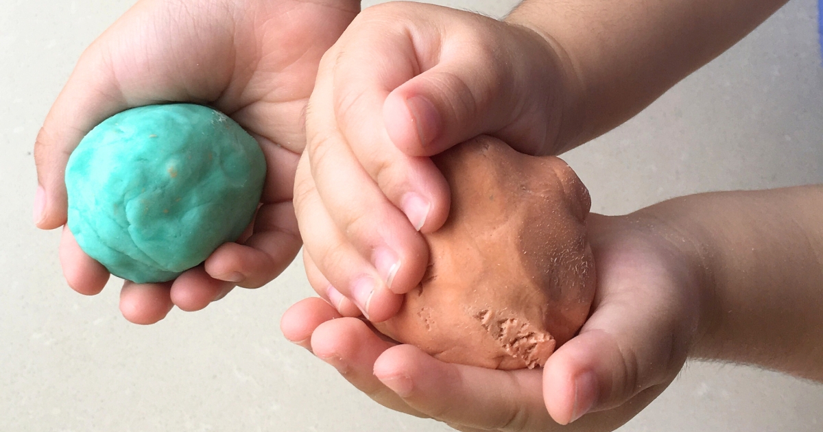 子どもの両手に、丸めた青緑色と茶色の粘土をのせている手元のアップ