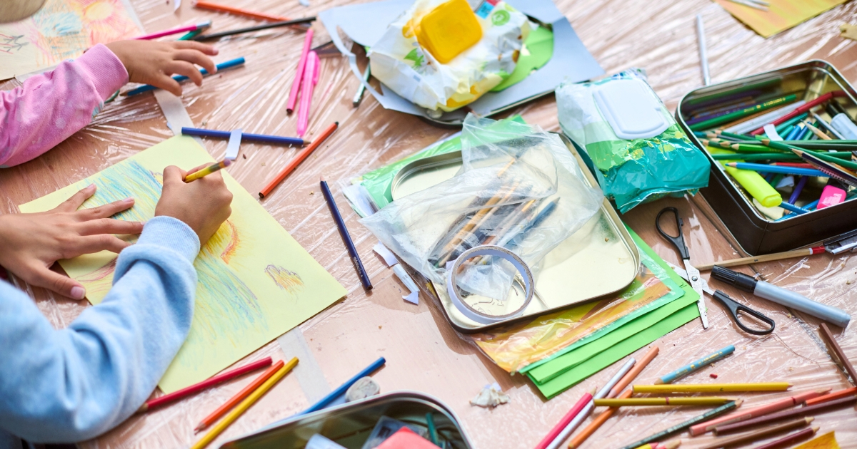 テーブルいっぱいに色鉛筆や工作道具が広がるなか、子どもが画用紙に絵を描いている様子