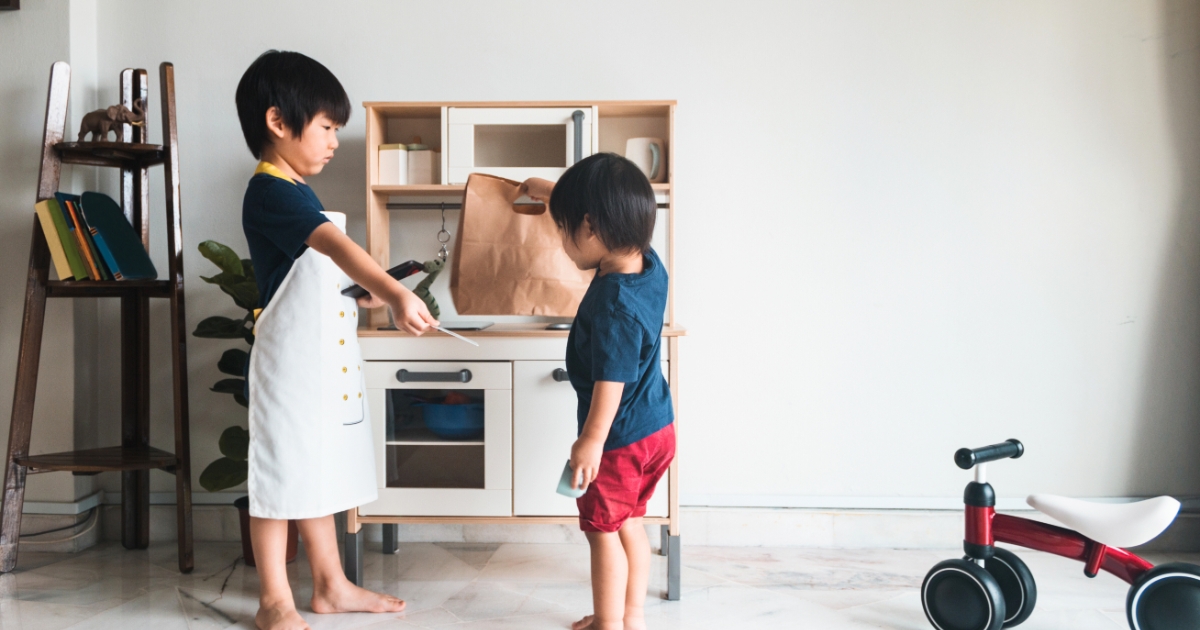 子ども2人が室内の木製キッチンでおままごとをしている。