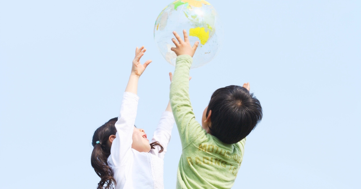 青空の下、子ども2人が地球柄の風船に手を伸ばして遊んでいる様子