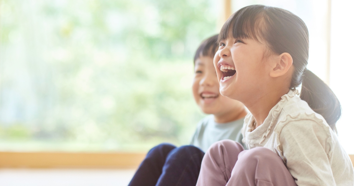 窓辺の明るい部屋で、笑顔ではしゃぐ女の子と後ろで微笑む男の子