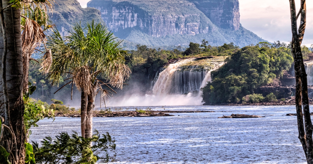 川の向こうに幅広い滝が流れ落ち、その背後に切り立った山々がそびえる南米の自然風景