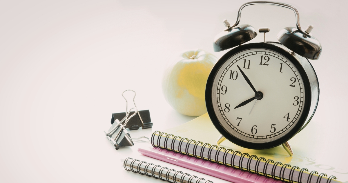 重ねられたノートと黒いダブルクリップの横に置かれた、黒いレトロな目覚まし時計