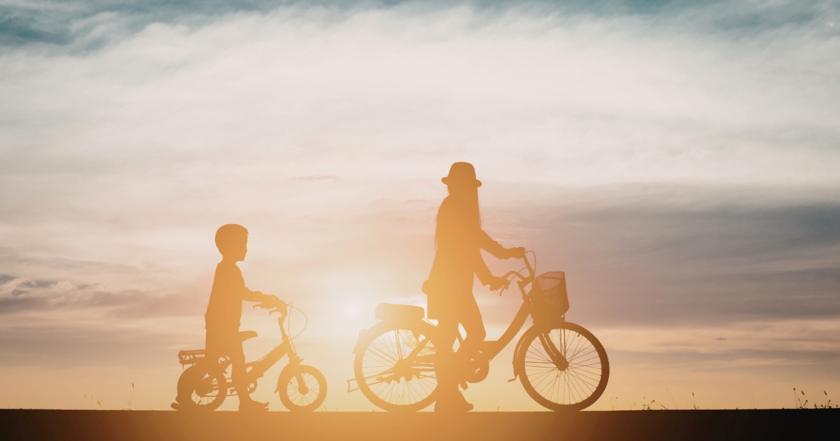 夕焼けの空を背景に、親子が自転車に乗って並んで走っているシルエット