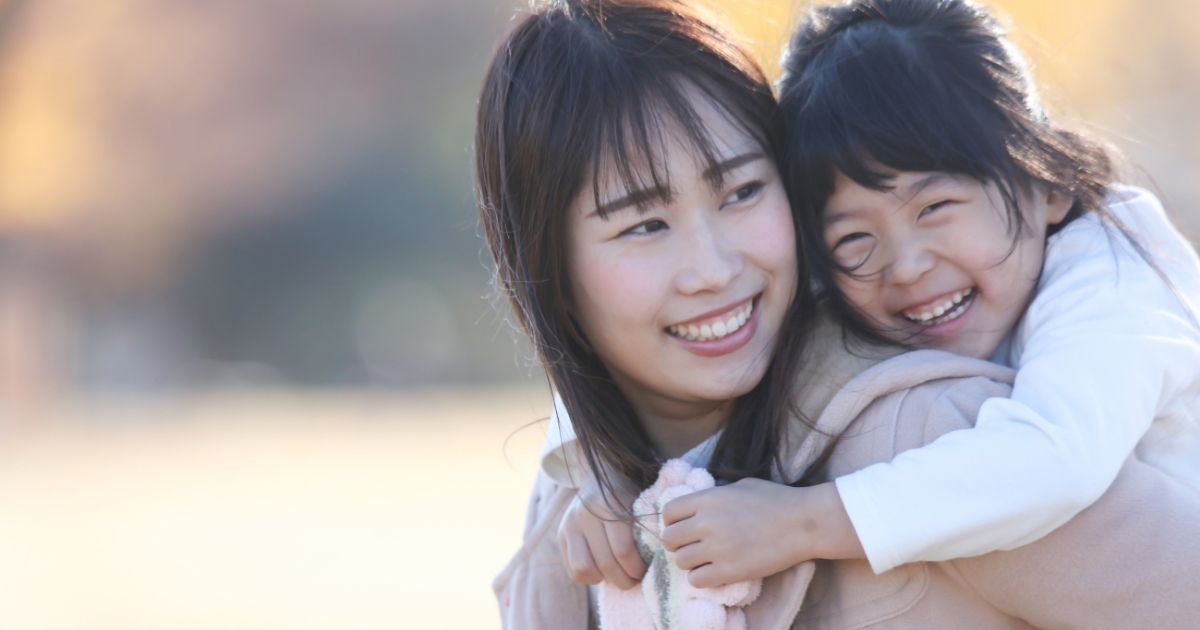 屋外で子どもをおんぶして笑顔を見せる母親