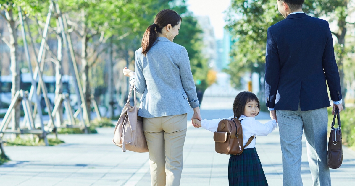 通学路で、両親と手をつないで歩くランドセルの女の子