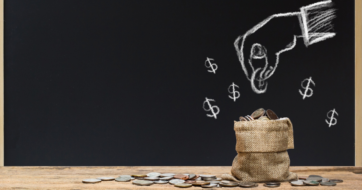 黒板に手がコインを落とすイラストとドル記号が描かれ、机の上には小銭と、コインが入った麻袋が置かれている様子