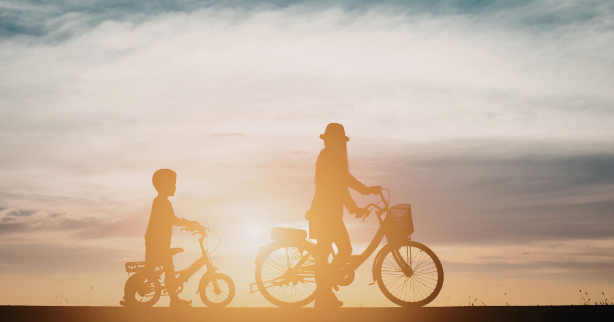 夕焼け空を背に、子ども2人が自転車に乗って並んで進むシルエットを写した、のびやかで穏やかな雰囲気の写真