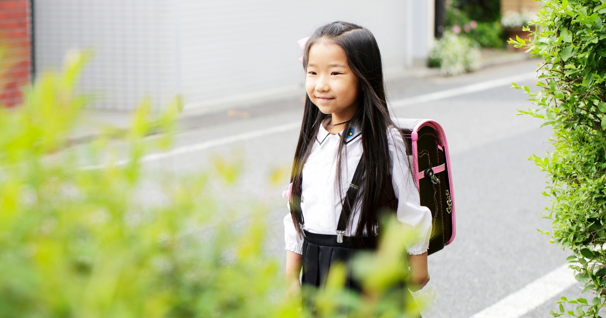 黒とピンクのランドセルを背負い、少し微笑みながら道を歩く小学生の女の子